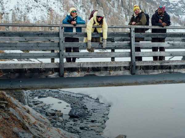 Vier Freunde geniessen die Aussicht von einer Holzbrücke aus, in einer verschneiten Landschaft