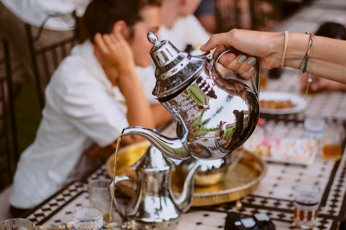 Eine Person schenkt Tee aus einer silbernen Teekanne ein