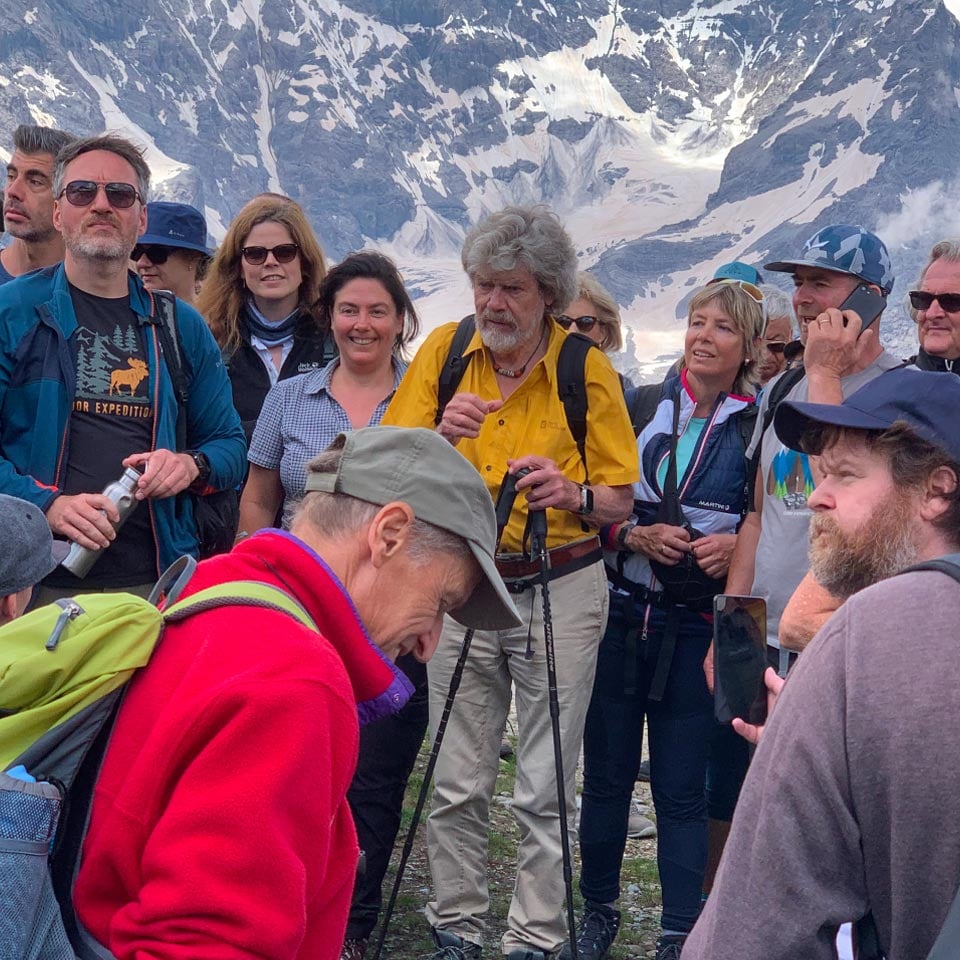 Mann in schwarzem Shirt steht vor einem Stand mit Outdoor-Bekleidung und Markenflaggen im Hintergrund