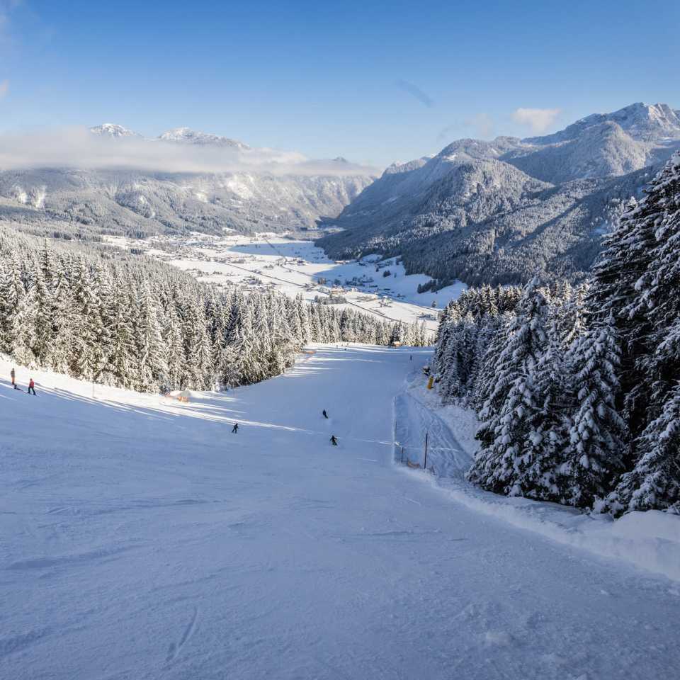 Winterliche Hornspitz-Abfahrt mit mehreren Skifahrern und Blick auf das verschneite Gosau im Tal, umgeben von bewaldeten Berghängen.