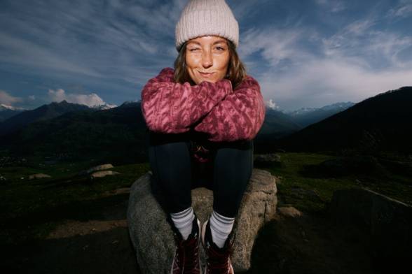 Junge Frau in sportlicher Wanderbekleidung hockt auf einem Felsen in der Dunkelheit