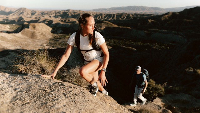 Eine Frau und ein Mann in sommerlicher Wanderkleidung klettern einen Felsen hinauf